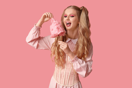 Beautiful young happy woman dressed as doll with cotton candy on pink background
