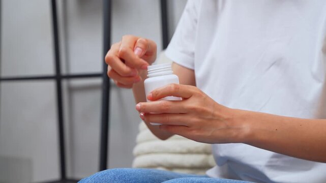 Woman sitting on sofa taking medication from a pill bottle at home, healthcare and treatment concept