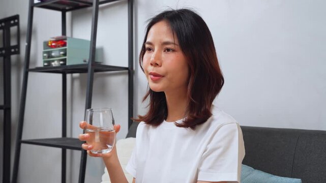 Happy Asian woman drinking a glass of water in the morning at home, healthy lifestyle and wellness concept