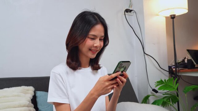 Asian woman using mobile phone for browsing and texting at home in a relaxed lifestyle moment.