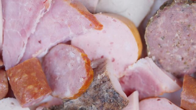 Closeup of assorted smoked and cured meat products under studio lighting. Assorted gourmet sausages and ham slices highlighted for highend food marketing and packaging