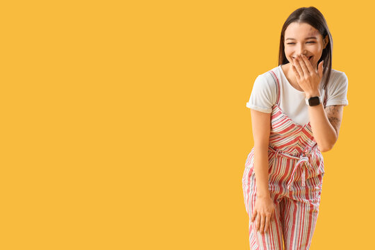 Young gossip woman laughing on yellow background