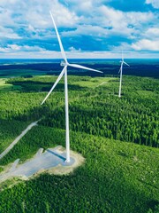 Aerial View of Wind Turbines Amidst Lush Green Forest Landscape Under Blue Sky in Finland © NBLX