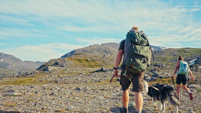 Middagsfjellet, Sandland, Nordkapp, Finnmark, Norway - Two Hikers, Accompanied by Their Dogs, Trek Across a Rugged, Rocky Landscape - Static Shot