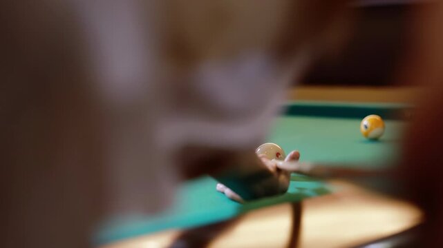 Young pool player hit the white cue ball with the cue to drives a orange american pool ball into the pocket of a green billiard table with smooth precise, sport activity indoors hobby and relax time
