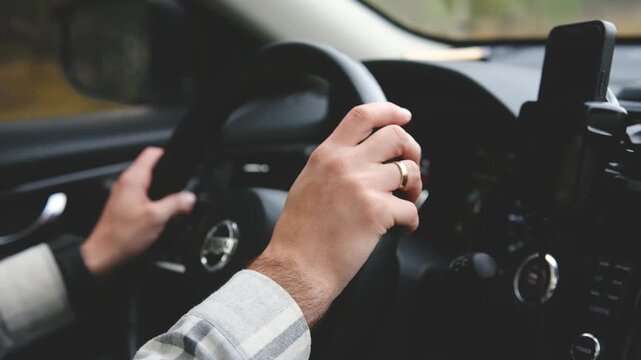 Person driving car, hands on steering wheel, wearing ring, nature background, forest trees
