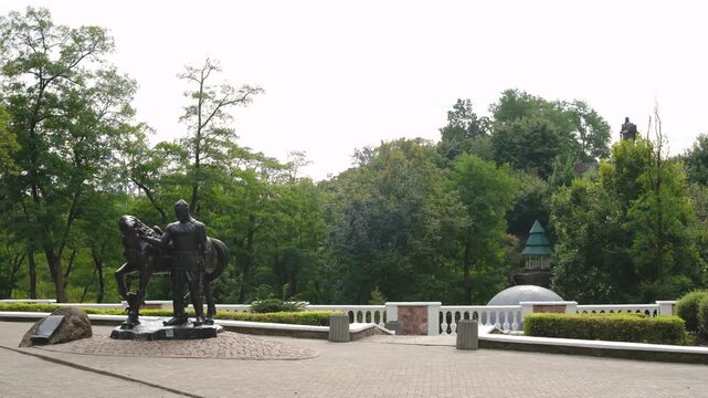 Bronze man and horse sculpture in a park with green trees and manicured bushes