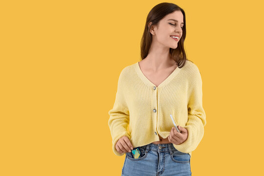 Young woman with credit card and mobile phone on yellow background