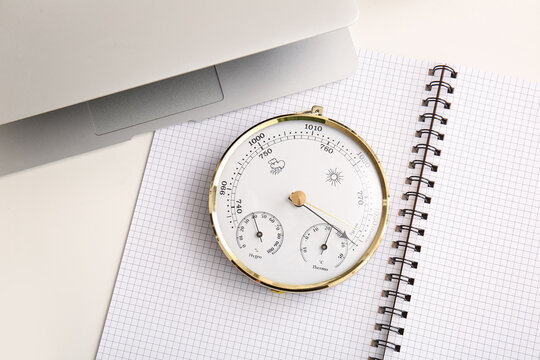 Notebook with aneroid barometer and modern laptop on white table, closeup