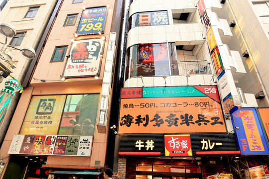 Vibrant commercial building facade in Shibuya district featuring Sukiya restaurant, Gyu-Kaku Izakaya, and colorful neon business signage for nightlife and dining - Tokyo, Japan, July 07, 2013