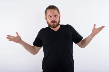 Fototapeta premium Studio portrait of a bearded young caucasian man with a hair bun wearing a black v-neck shirt. He is shrugging his shoulders with a confused expression, isolated on a white background.