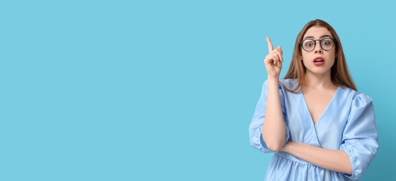 Thoughtful young woman pointing at something on blue background with space for text