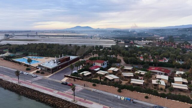 411
Taiga Resort,L&rsquo;Ampolla,Tarragona,Catalonia,Spain,Delta de L&rsquo;Ebre,Costa Dorada, reveal drone flight of rice paddies and campsite showing resort and seafront with mountains beyond interesting sky