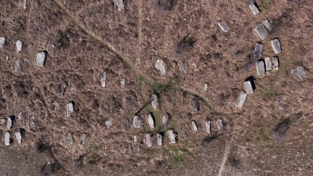Top-down drone shot of scattered medieval tombstones (stecci) across a dry landscape, revealing historic burial patterns in Herzegovina.