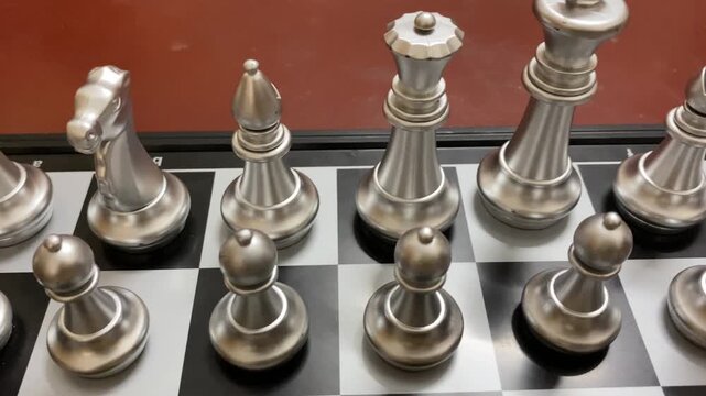 Indoor game: Silver colored chess pieces arranged on a board, ready to start game.