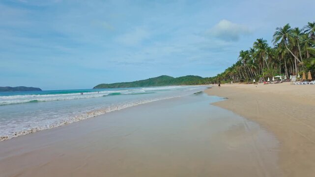 Seaside stroll past palm lined coast with swimmers and calm ocean atmosphere