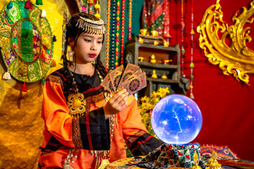Obraz premium Fortune teller woman in Bohemian costume and headdress holding taro cards felling fortune prediction in Moroccan style room