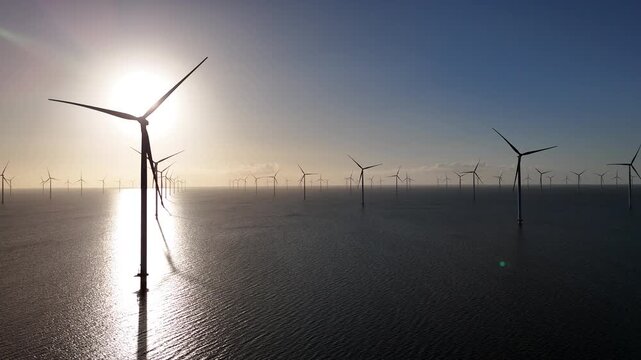 Diagonal aerial view over offshore wind farm in backlight