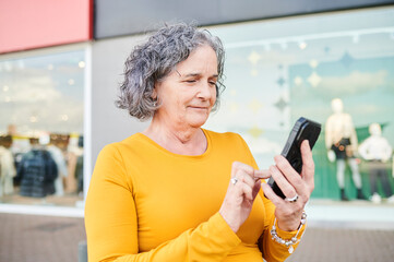 Fototapeta premium Senior woman using smartphone for shopping in city