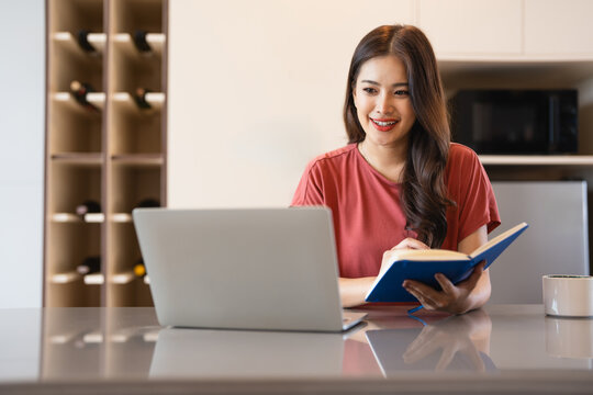 Happy thoughtful remote employee, working at laptop form home, looking at window away, thinking over workday tasks. Student making notes at kitchen table, sitting at computer in deep thoughts.