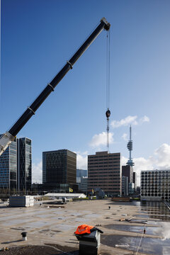 View from a flat rooftop featuring a construction crane  with modern office buildings in the background. Clean urban skyline under sunny skies with scattered clouds, representing business growth