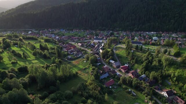 Aerial view of rural village in Orava region, Slovakia, surrounded by green hills and forest in warm sunset