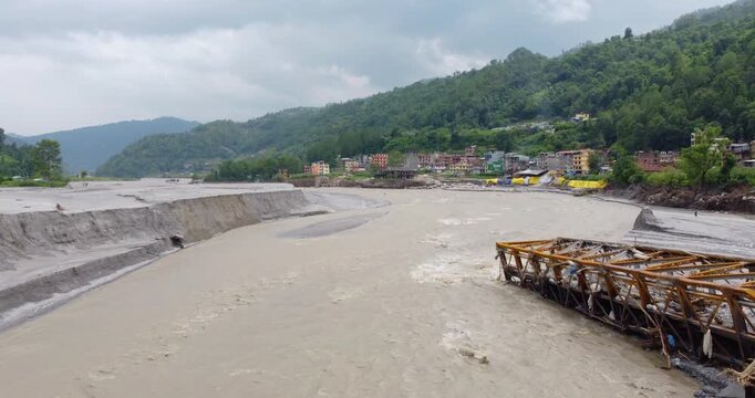 Drone shot of a collapsed bridge on the Melamchi River with eroded riverbanks impacting nearby residential areas after severe flooding in Nepal.