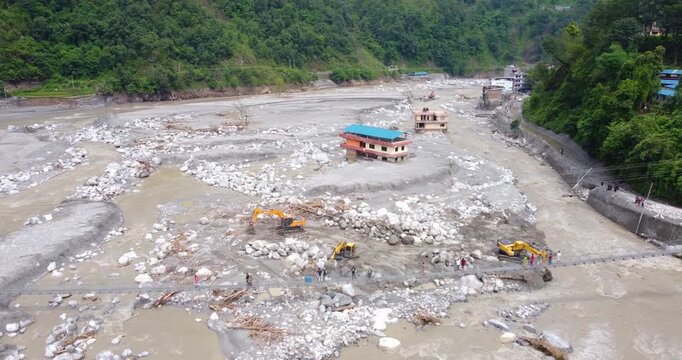 Drone shot of Melamchi aftermath showing houses buried in sand and an excavator working along the riverbank after severe flooding in Sindhupalchowk, Nepal.