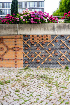 Daylight reveals brick wall mosaic pattern and texture with cobblestone ground and urban garden flowers creating vibrant courtyard detail