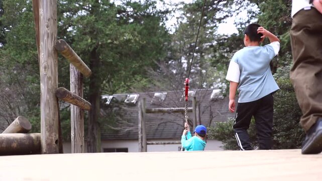 Slow motion of a boy playing on a zip line or rope swing at an outdoor adventure park, rear view.