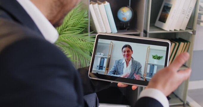 Business man in suit looking at tablet screen having online webinar, video call or conference with cheerful young female colleague sitting in office. Concept of internet communication. 4k video.
