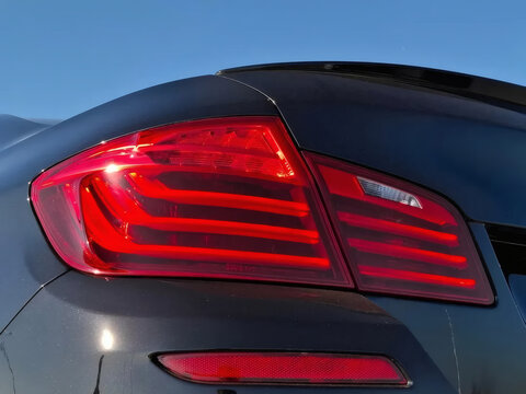 Close-Up Of Red LED Car Taillight On Glossy Black Rear Panel With Sunlit Reflection