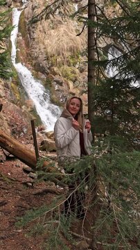 A woman against the backdrop of a mountain waterfall.