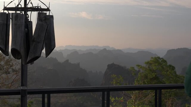 Layered karst mountains in the background, static shot as man approaches handrail and admires the view.