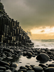 Obraz premium Atmospheric Basalt Formations Under Dramatic Skies and Ocean Spray