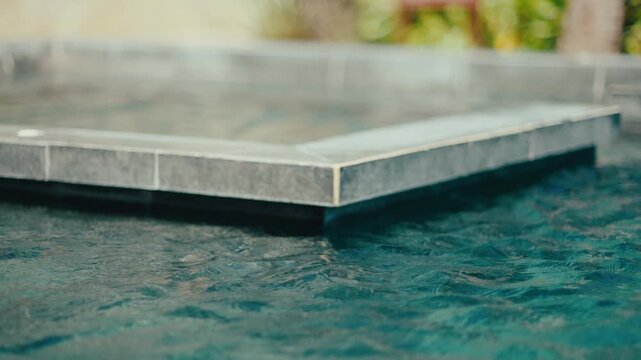 Calm blue resort pool edge with tiled infinity-style detail, gentle ripples and relaxing vacation atmosphere.