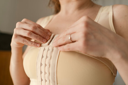 A woman fastens her postoperative compression bra. Close-up of the closure system ensures proper fit for recovery after breast reconstruction.