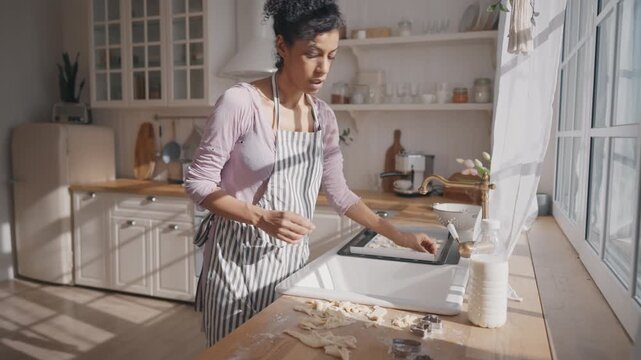 Happy housewife cooking alone at home kitchen, singing and dancing, medium shot. African american single woman enjoying calmness and solitude in sunday morning, doing housework and feeling good