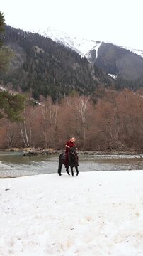 A woman on a horse in the snowy mountains with a mountain river in the background. Excursion, mountain trip.