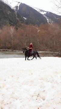 A woman on a horse in the snowy mountains with a mountain river in the background. Excursion, mountain trip.