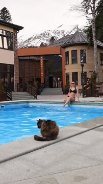 A girl relaxes near the pool with her cat against the backdrop of a snowy mountain.