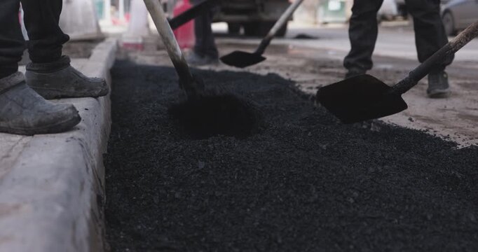 Workers shoveling fresh asphalt along roadside