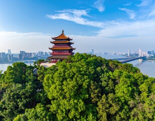 Obraz premium An aerial view showcases a traditional Chinese pagoda perched atop a lush green hill, overlooking a sprawling cityscape and a modern suspension bridge against a vibrant blue sky.