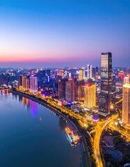 Obraz premium An aerial view showcases a vibrant cityscape illuminated at dusk, with a river winding through the urban landscape and a stunning sunset painting the sky with warm hues.