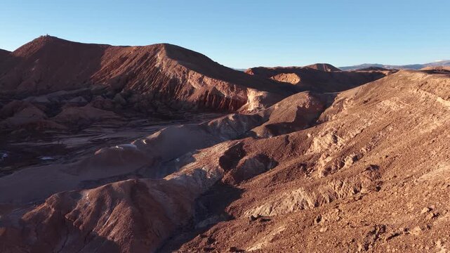 Cinematic drone shot flying forward along the sharp edge of a rocky ridge in Mars Valley (Valle de Marte), revealing the rugged, red terrain of the Cordillera de la Sal at sunset