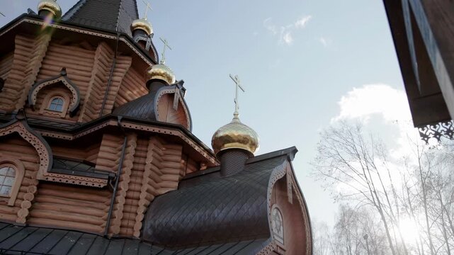 Low angle perspective capturing intricate details of a traditional wooden church exterior. Multiple golden onion domes topped with gleaming crosses reflect sunlight against a bright blue sky. Rich tex