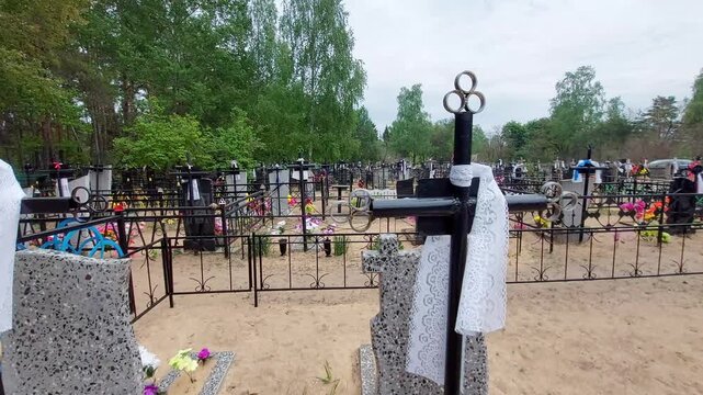 Expansive view of Orthodox cemetery on Radonitsa holiday, rows of grave sites decorated with flowers and traditional white lace on crosses, sandy pathways, serene atmosphere of remembrance