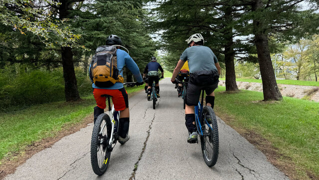 Group mountain bikers riding on a tree-lined paved park path with backpacks and helmets