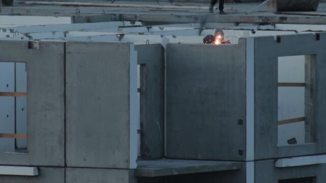 Close up view of worker performing welding operation on precast concrete building panels during construction site activity sparks fly from connection point assembly process