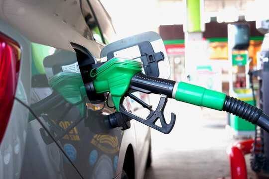 Fuel nozzle inserted into car tank at gas station, green handle close-up. Transportation energy concept with refueling process, modern vehicle detail and clean industrial environment.